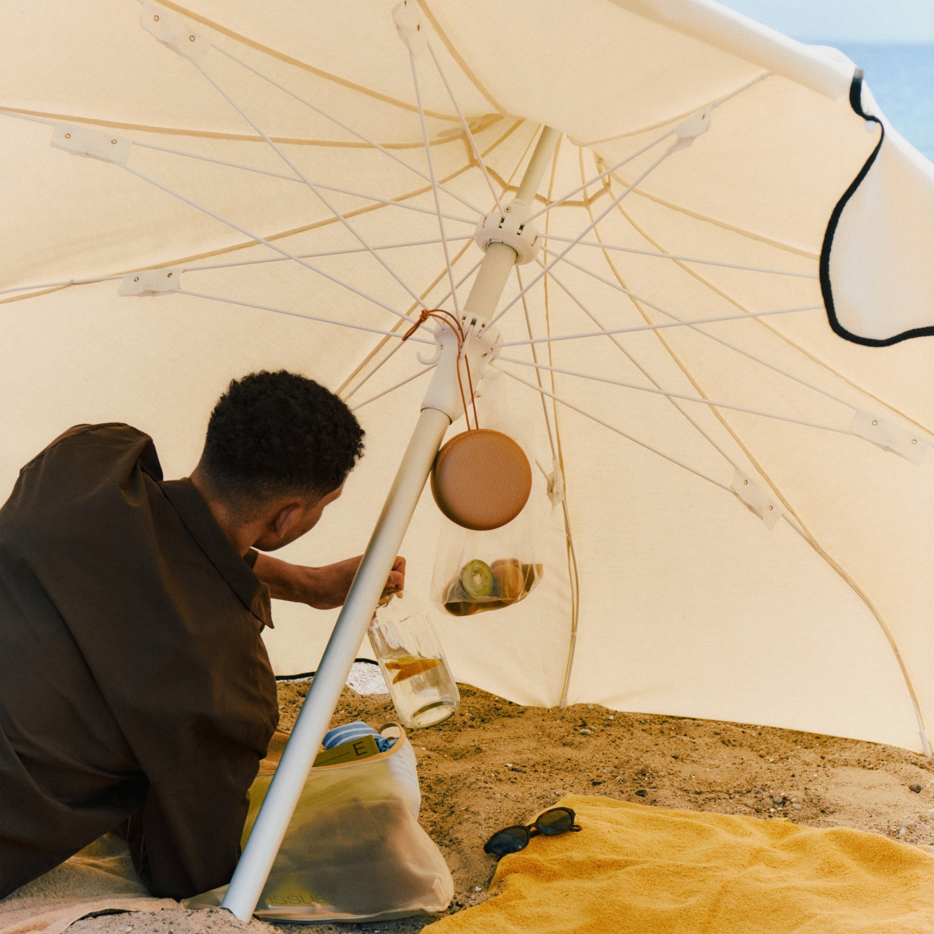 Bang & Olufsen B&O Beosound A1 3. Generation in der Farbe Honey Tone an einem Sonnenschirm hängend