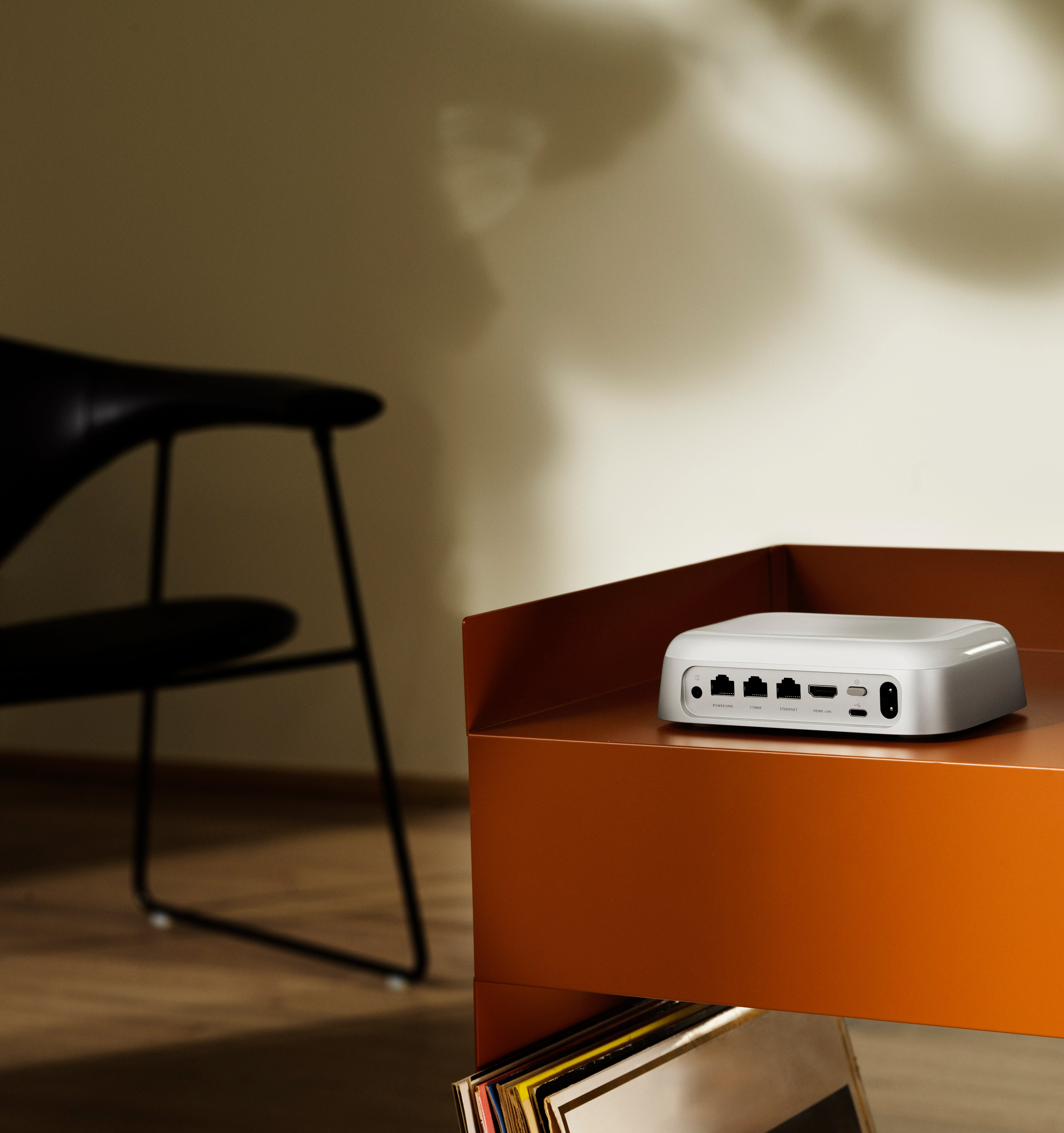 Lifestyle-Nahaufnahme der Rückseite des Bang & Olufsen Beoconnect Core. Das Bild zeigt das übersichtliche Anschlusspanel mit HDMI eARC, Powerlink, Ethernet und USB-C auf einem modernen, terracottafarbenen Regal. Es verdeutlicht die einfache Verkabelung und das minimalistische Design des Streaming-Hubs.