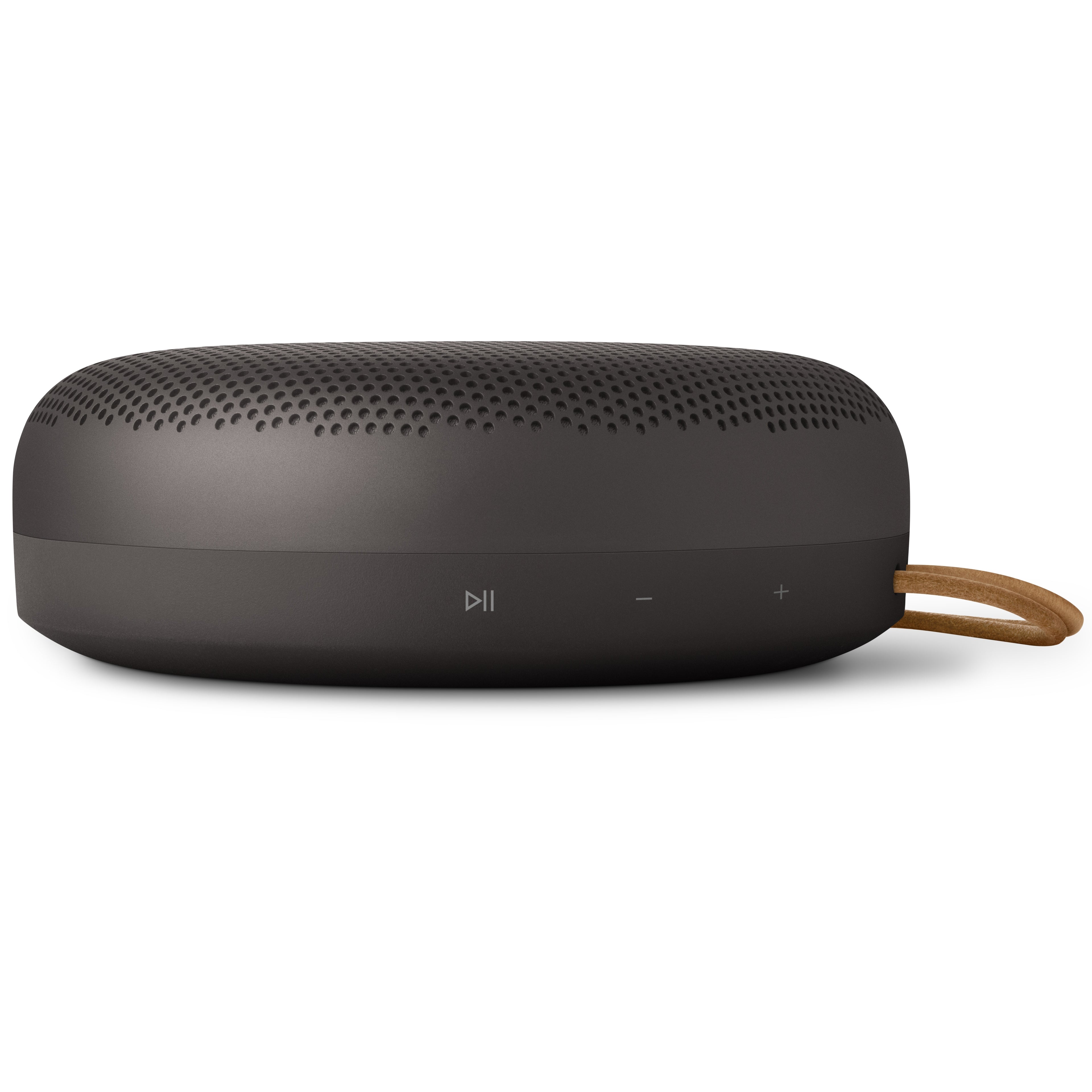 Seitenansicht des Bang & Olufsen Beosound A1 Lautsprechers in Anthrazit mit Fokus auf die integrierten Bedienelemente für Wiedergabe/Pause sowie Lautstärkeregelung (Plus/Minus Symbole) am unteren Gehäuserand.