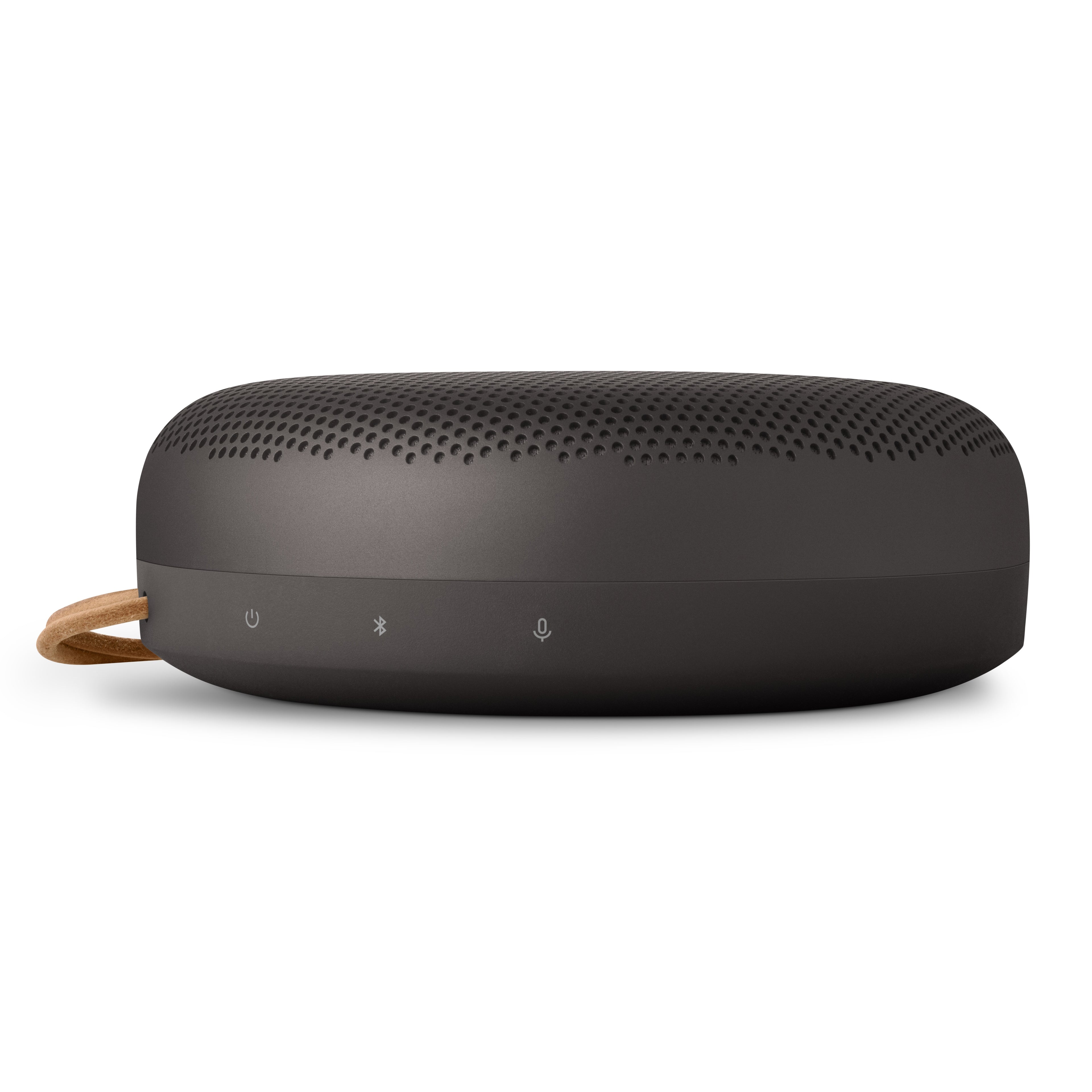 Seitenansicht des Bang & Olufsen Beosound A1 in Anthrazit mit Fokus auf die Symbole für Power, Bluetooth-Pairing und Sprachassistent/Mikrofon auf dem gummierten Sockel unterhalb des Aluminium-Gitters.