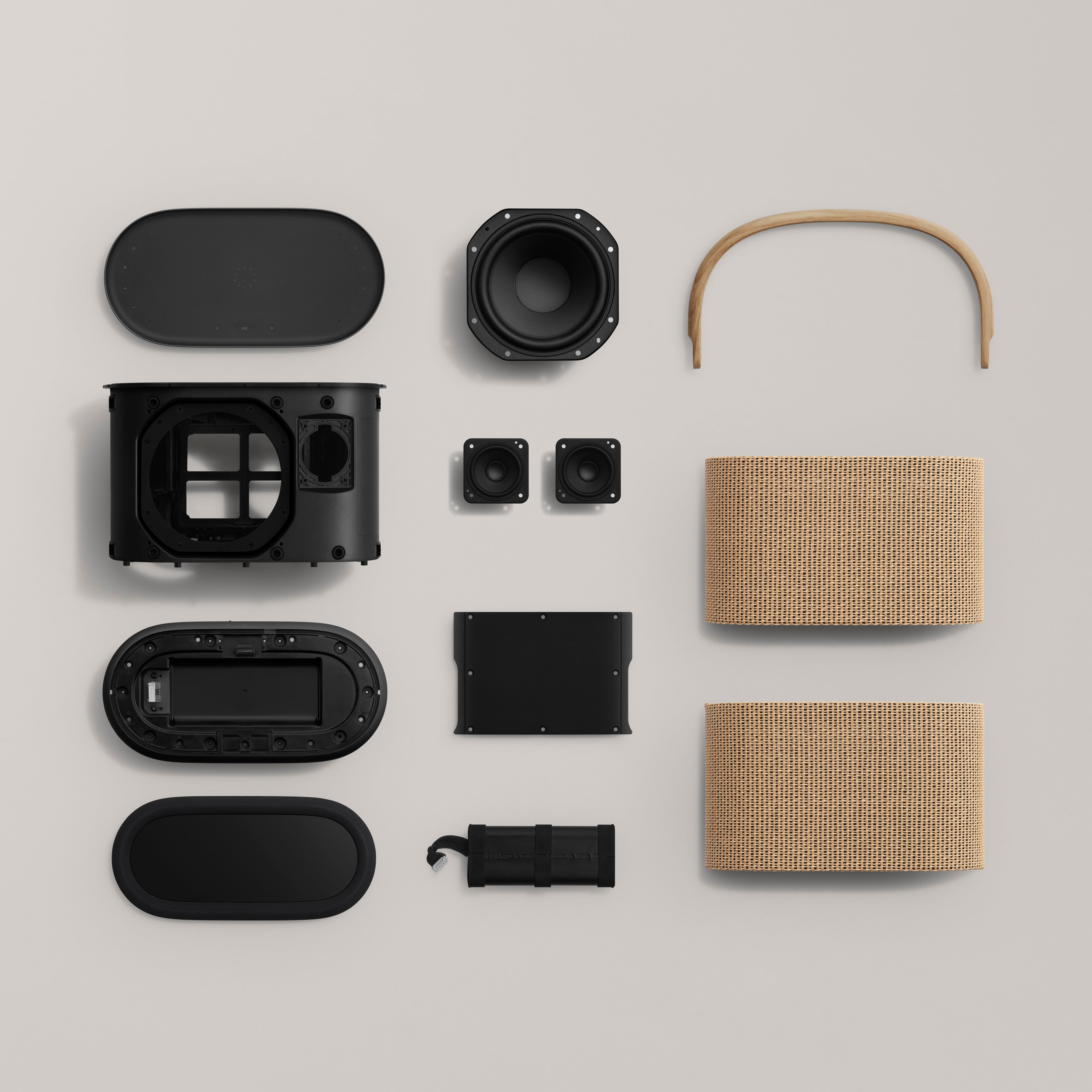Modulares Design des Bang & Olufsen Beosound A5: Eine strukturierte Übersicht der Einzelkomponenten, darunter das Gehäuse, Lautsprechertreiber, der Eichenholz-Griff, die Nordic-Weave-Frontabdeckungen und der austauschbare Akku auf hellem Hintergrund.