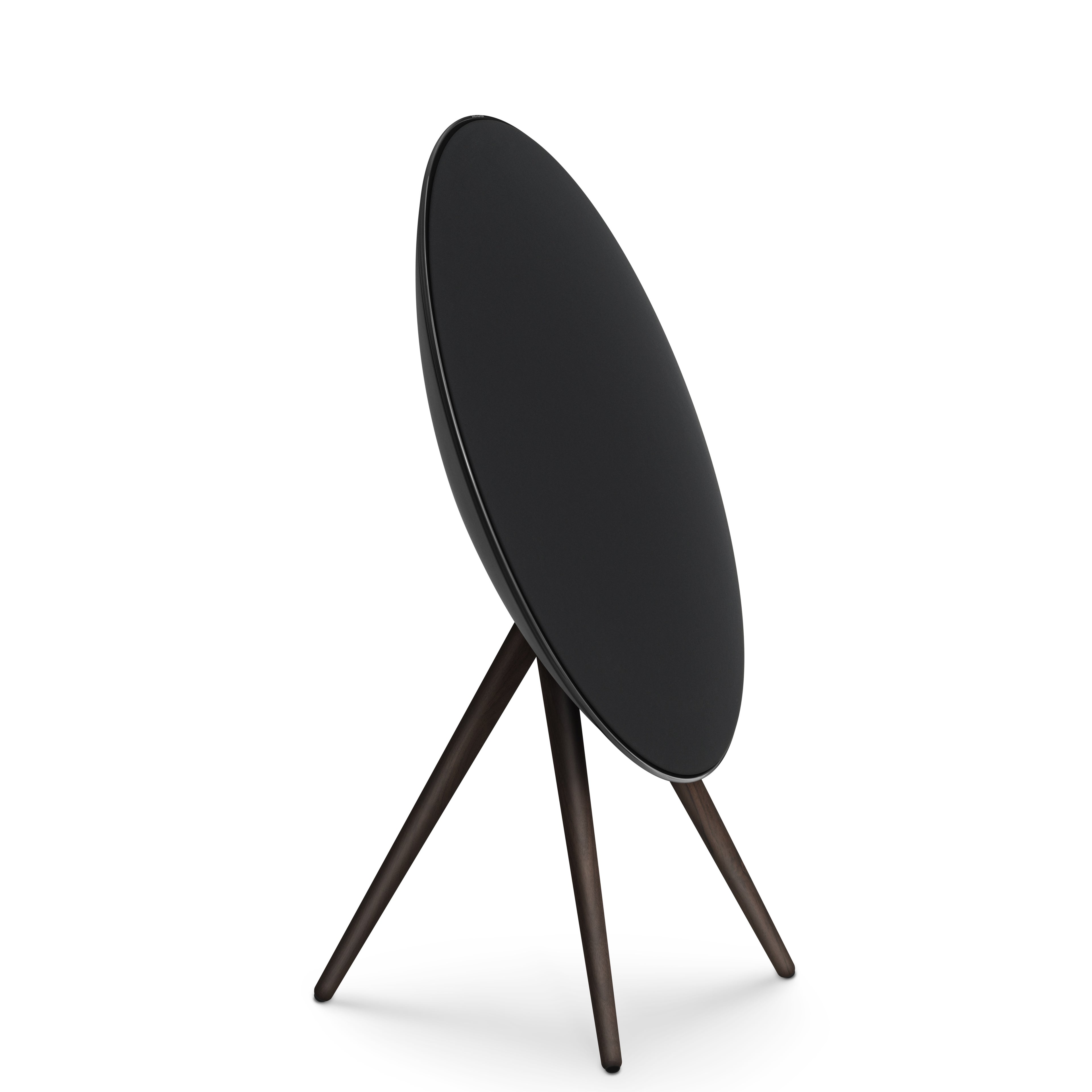 Seitenprofil (3/4-Ansicht) der Bang & Olufsen Beosound A9 in der Ausführung Black Anthracite. Der Lautsprecher präsentiert sich mit einem schwarzen Aluminiumring, einer passenden schwarzen Textilfront und Stativbeinen aus dunklem Nussbaumholz. Ein kraftvolles und monolithisches Design-Statement, freigestellt auf weißem Hintergrund.