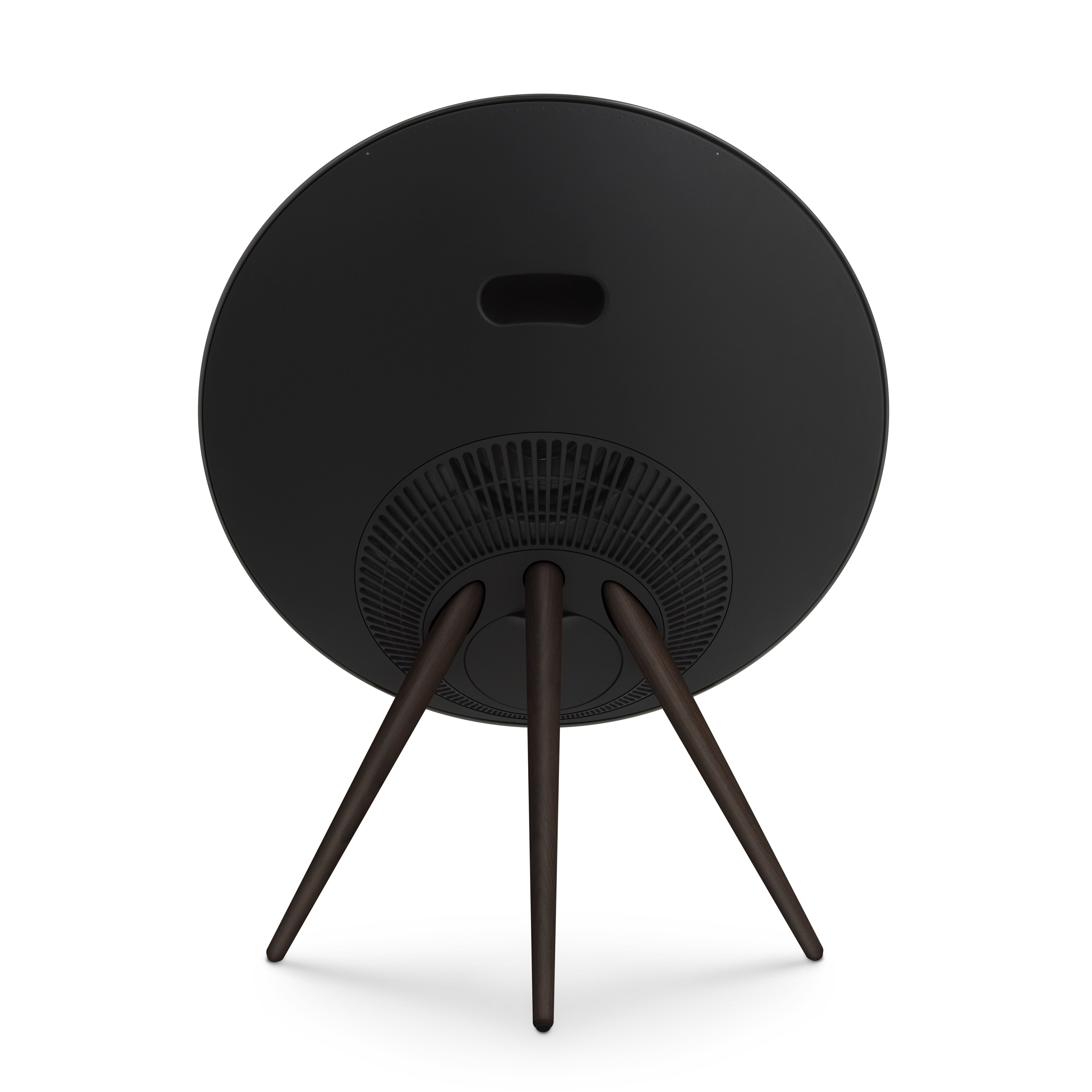 Zentrale Rückansicht der Bang & Olufsen Beosound A9 in Black Anthracite. Das Bild zeigt das nahtlose, schwarze Rückgehäuse mit dem ergonomischen Tragegriff, die kreisförmig angeordneten Belüftungsschlitze und die stabilen Stativbeine aus dunklem Nussbaumholz. Professionelles Produktfoto, freigestellt auf weißem Hintergrund.