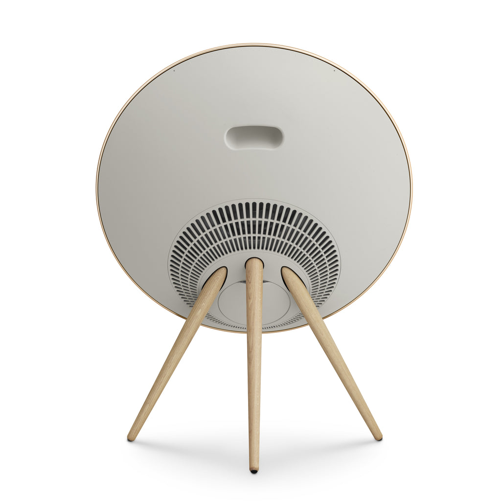 Die Rückseite der Beosound A9. Gezeigt wird das minimalistische weiße Gehäuse mit integriertem Tragegriff und der eleganten Kabelführung zwischen den Holzstativen.