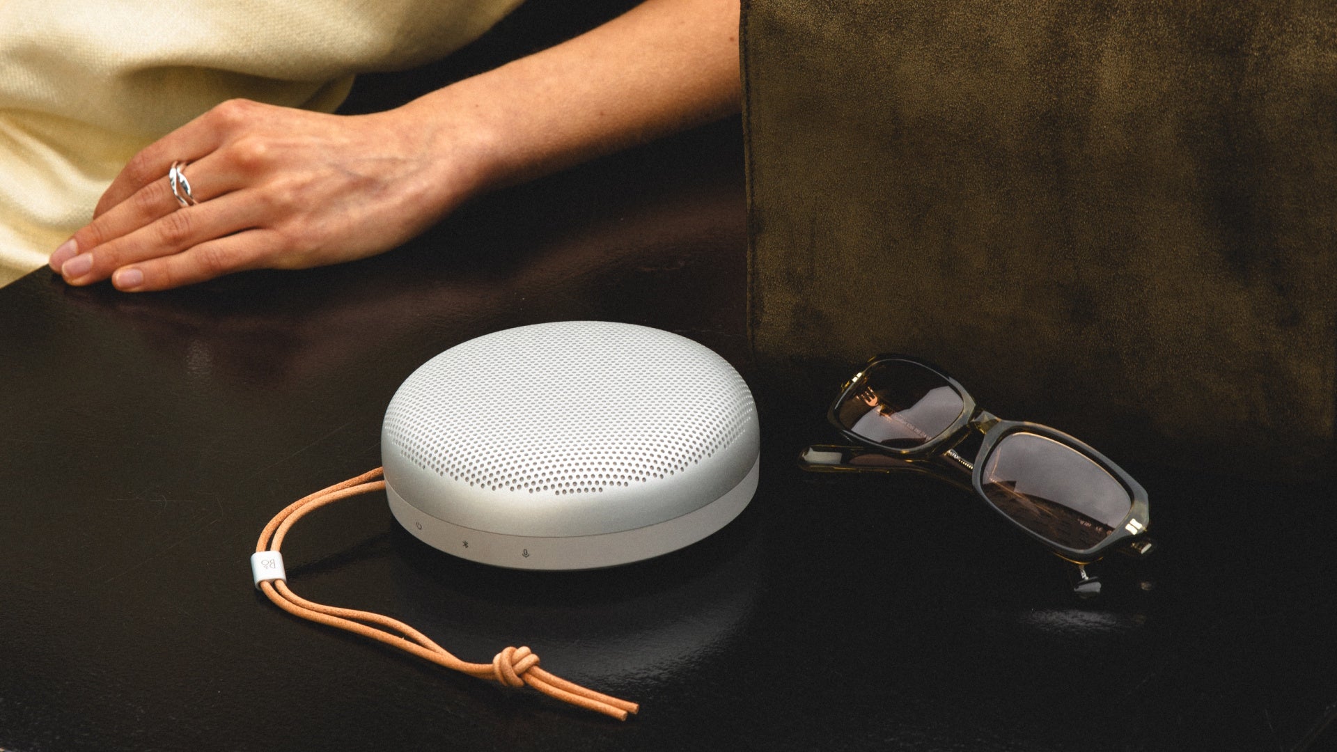 Bang & Olifsen, B&O Beosound A1 (3. Generation)  in Natural Aluminium auf einer Bank neben einer Sonnenbrille