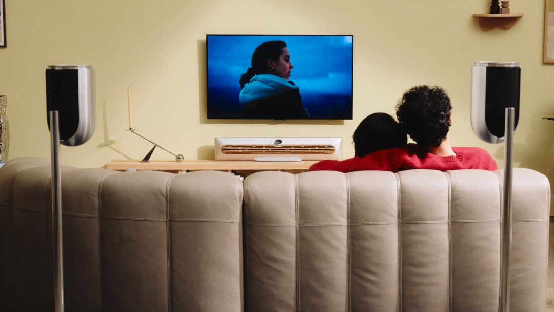 Wohnzimmer mit einem TV an der Wand darunter Beosoudn Premiere Soundbar auf einem Sideboard und Beolab 8 als Rear Speaker auf Bodenstandfüßen