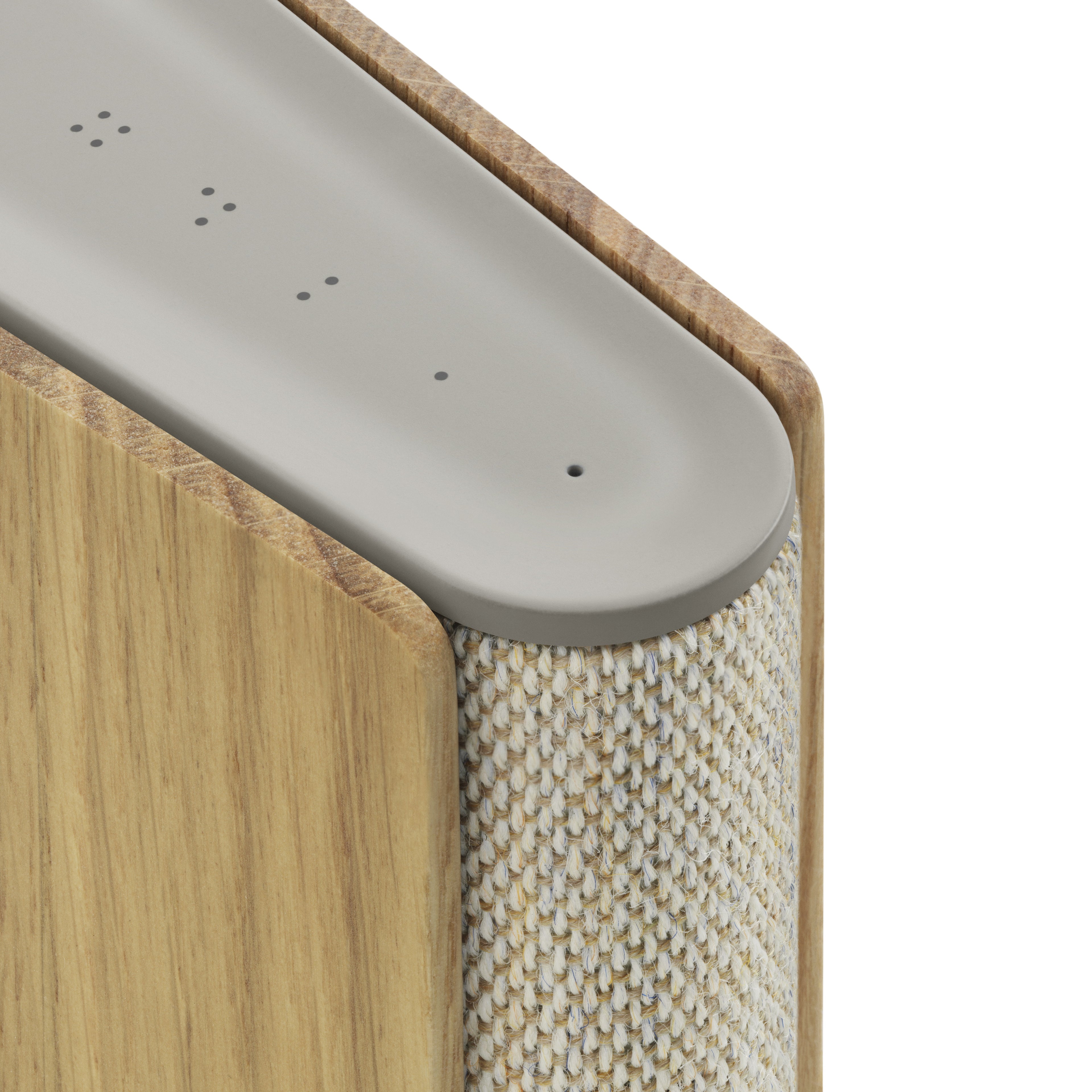 Detailaufnahme der oberen Rückseite der Bang & Olufsen Beosound Emerge. Gezeigt werden die vier haptischen Favoritentasten (Punktsymbole) auf der Soft-Touch-Oberfläche sowie der präzise Übergang zwischen der Eichenholz-Wange und dem melierten Textilrücken.